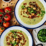 Cream of broccoli soup served in two white bowls on a wooden board.