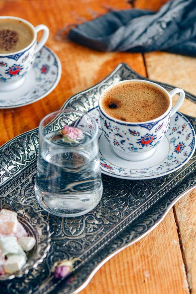 Turkish coffee in traditional cups served on a traditional copper tray with a small glass of water on the side.