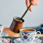 用手将土耳其咖啡从铜咖啡壶倒入传统的小咖啡杯中。土耳其软糖在旁边。
