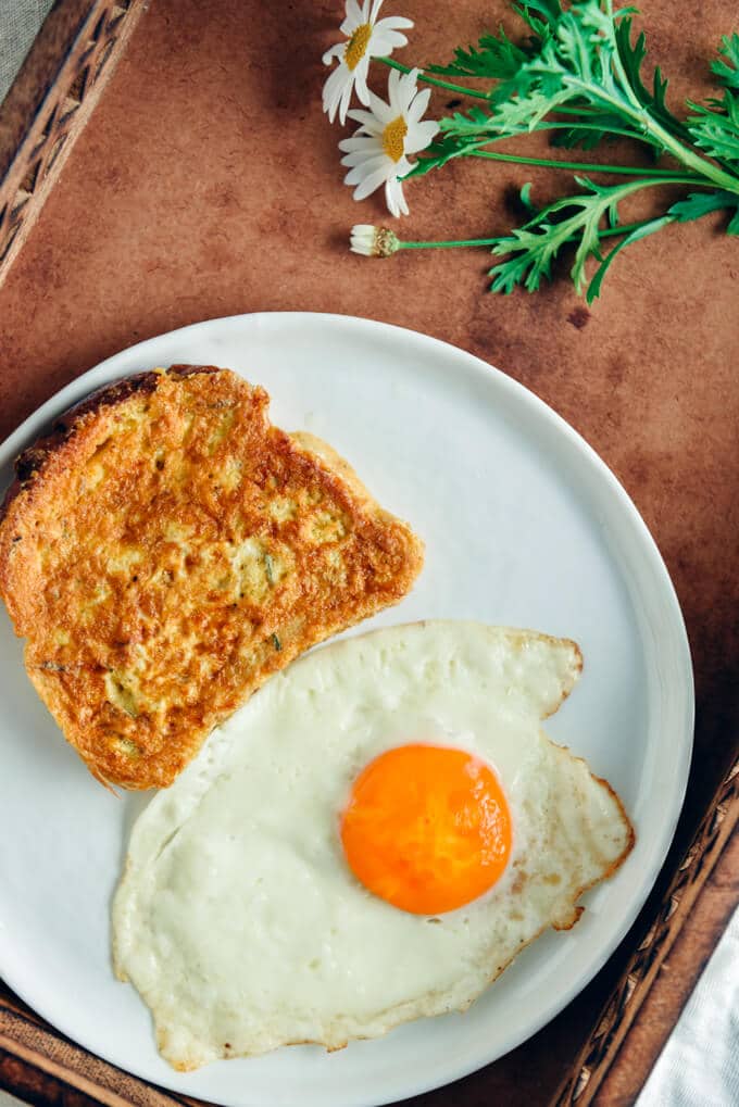 白色盘子上的法式吐司，旁边放着一个煎蛋，从俯视图拍摄，春天的鲜花陪伴着早餐。