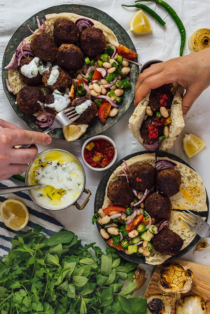 Homemade Turkish Meatballs are spicy, tender and perfectly juicy. It’s not a secret any more to make meatballs at home. #turkishfood #meatballs #meatballsrecipe #middleeasternfood #kofta #kofte 手握正宗的土耳其肉丸与叉子和三明治,豆沙拉,漆树阴离子,土耳其cacik和柠檬楔子陪伴。