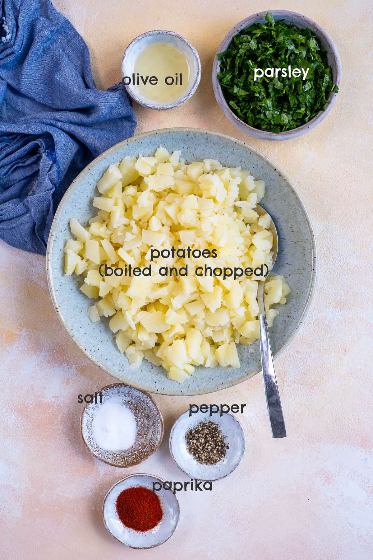切碎的煮土豆放在碗里，欧芹、橄榄油、盐、胡椒和红辣椒放在不同的碗里，背景要淡。