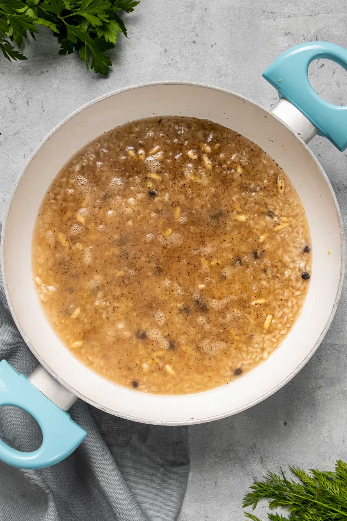 洋葱,松子,大米,香料和醋栗加水在白色平底锅里煮。