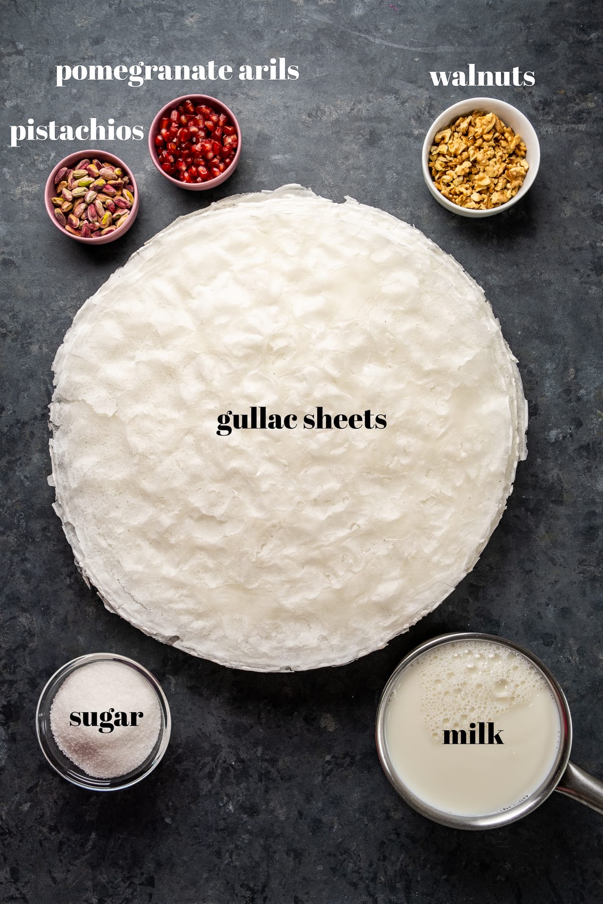 Gullac床单包围开心果、石榴假种皮、核桃、糖和牛奶在单独的碗在一个黑暗的背景。