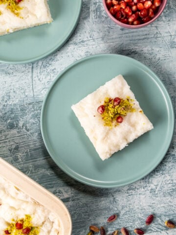 A slice of gullac dessert on two pastel colored plates on a light background, a bowl of pomegranate arils on the side.