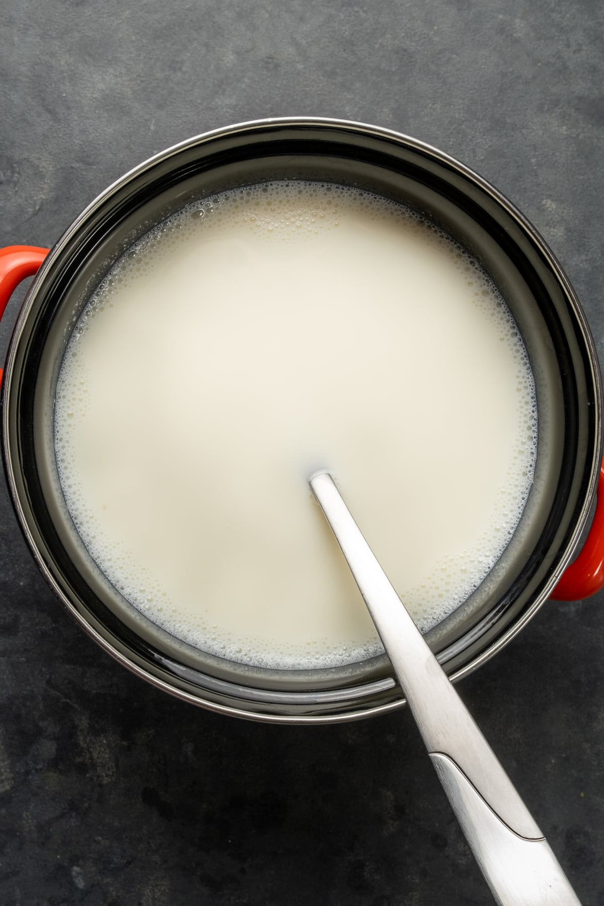 热牛奶在锅里，勺子在锅里，黑色背景。