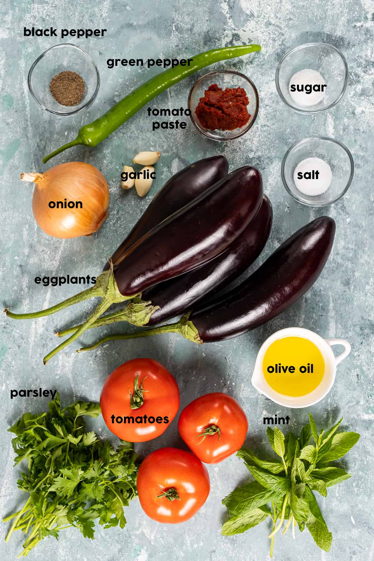 把茄子、青椒、洋葱、欧芹和薄荷、橄榄油、大蒜、番茄酱和香料放在小碗里，放在灰色的背景上。