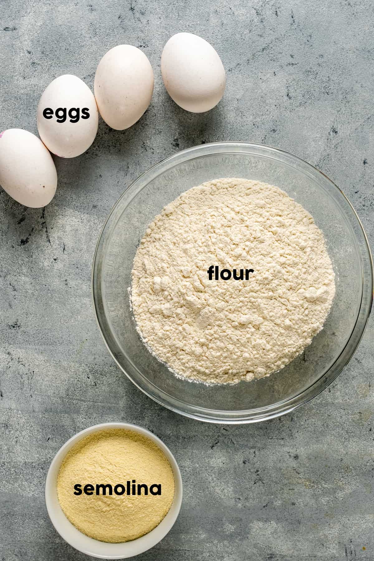 面粉在大碗里，粗面粉在小碗里，鸡蛋在灰色的背景上。