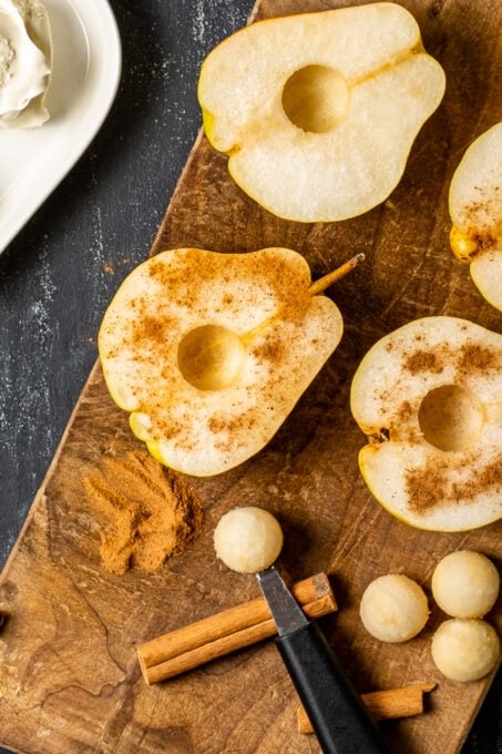把梨切成两半，去核，涂上肉桂粉，放在木板上，旁边放一个打瓜器和肉桂棒。