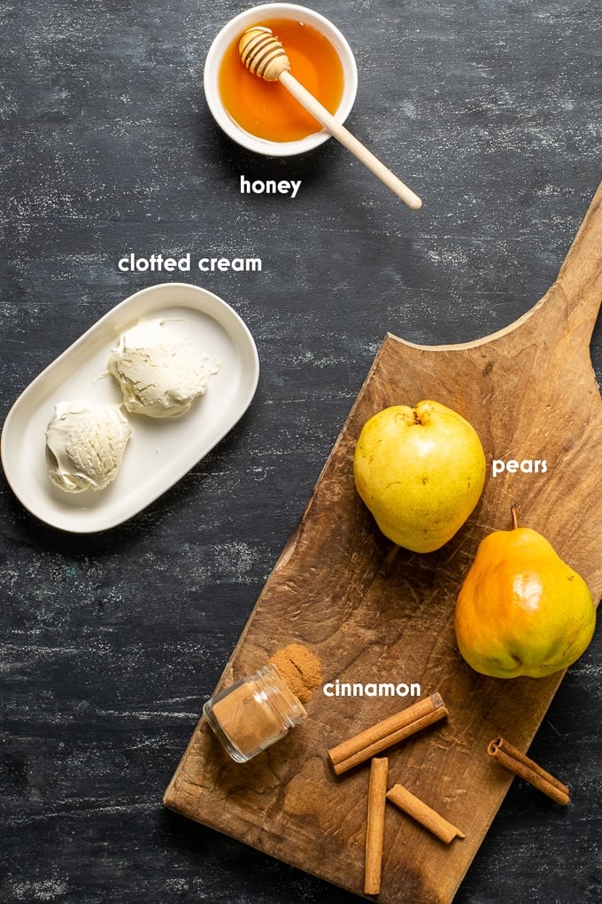 两个梨，肉桂粉放在一个小罐子里，肉桂棒放在木板上，黑色背景上有凝固的奶油和蜂蜜。