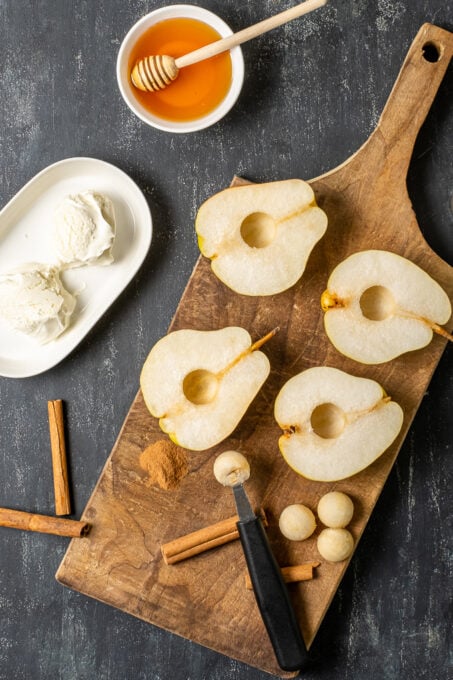 梨子切成两半，放在木板上，肉桂棒，打瓜器，奶油和蜂蜜放在旁边。