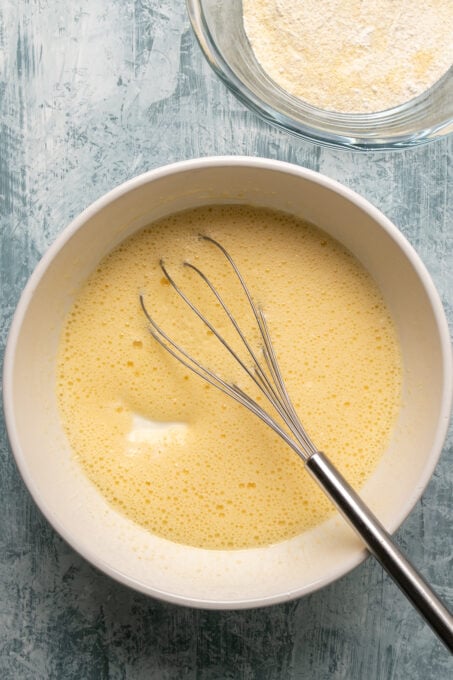 酸奶和石油添加鸡蛋糖的混合物在一个白色的碗和一只手打在里面。