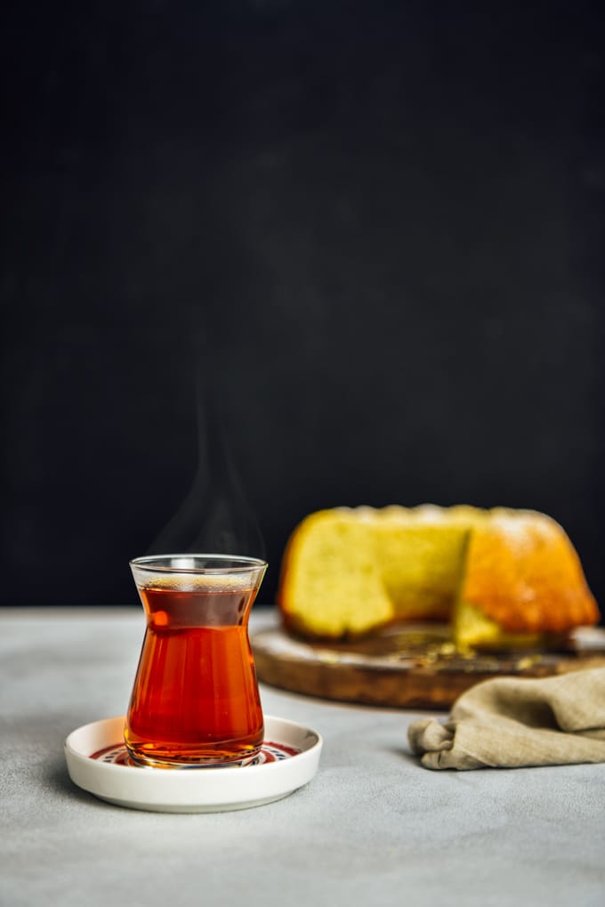 热腾腾的土耳其茶盛在传统的土耳其茶玻璃杯里，放在茶盘上，从正面拍摄，背景为深色。配上柠檬蛋糕。