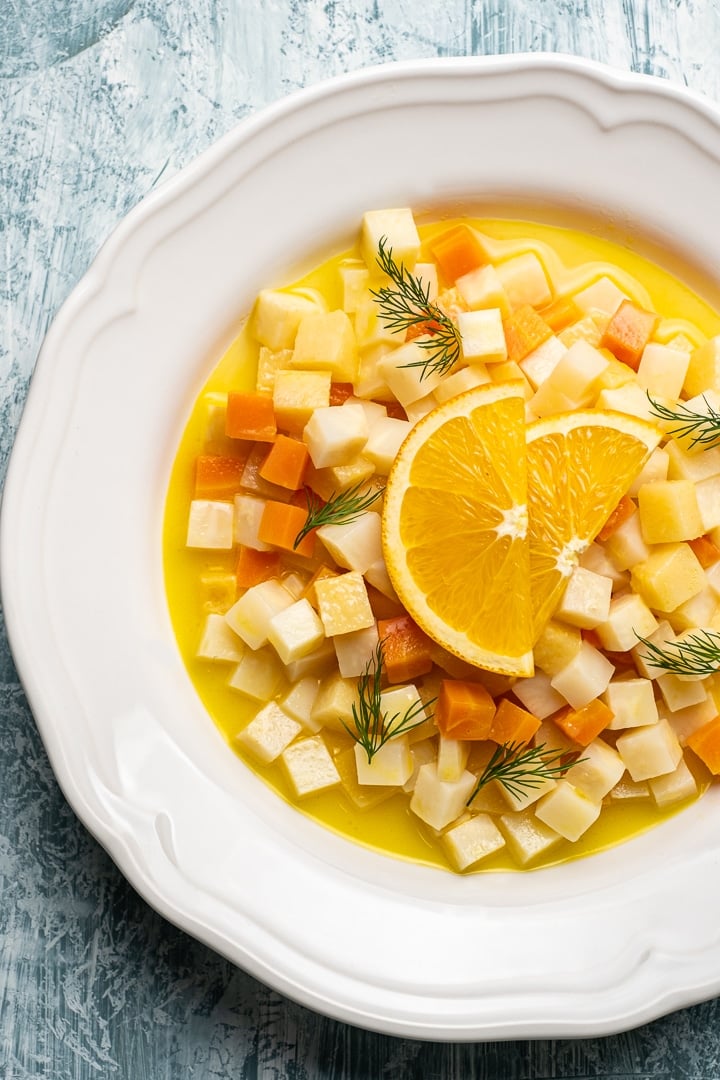 这是一款素食块根芹的食谱，用胡萝卜、木瓜和柑橘汁在白色的圆形盘子里浇上橘子角。