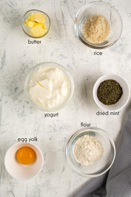 酸奶、蛋黄、面粉、薄荷干、米饭和黄油放在不同的碗里，背景为白色。