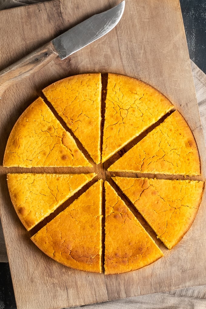 在圆锅里烤的热水玉米面包，在木板上切成薄片，旁边有一把刀。