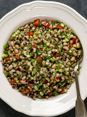 黑眼豆豆沙拉配香草，洋葱和甜红辣椒在一个白色的盘子里，里面放一个勺子。