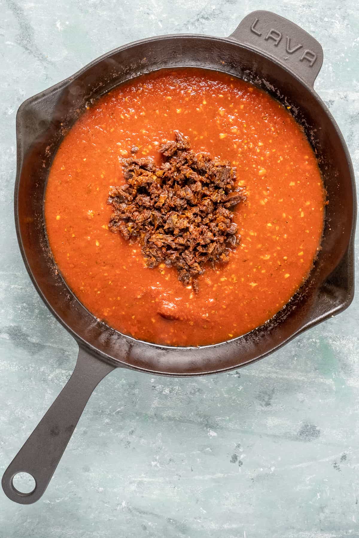剁碎的晒干的番茄在辣味番茄酱在铸铁煎锅。