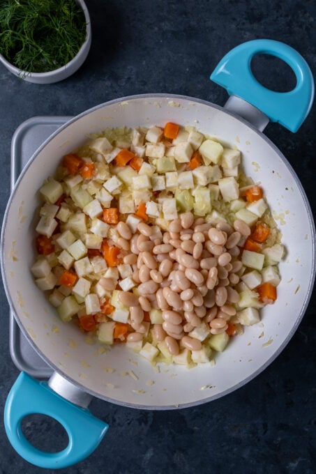 煮熟的豆在一块白色的平底锅中添加了切片的芹菜根，红萝卜和苹果。
