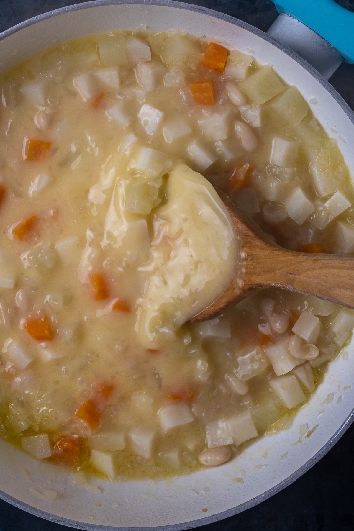 Celeriac和苹果汤用在一个白色平底锅和在它里面的一把木匙子。
