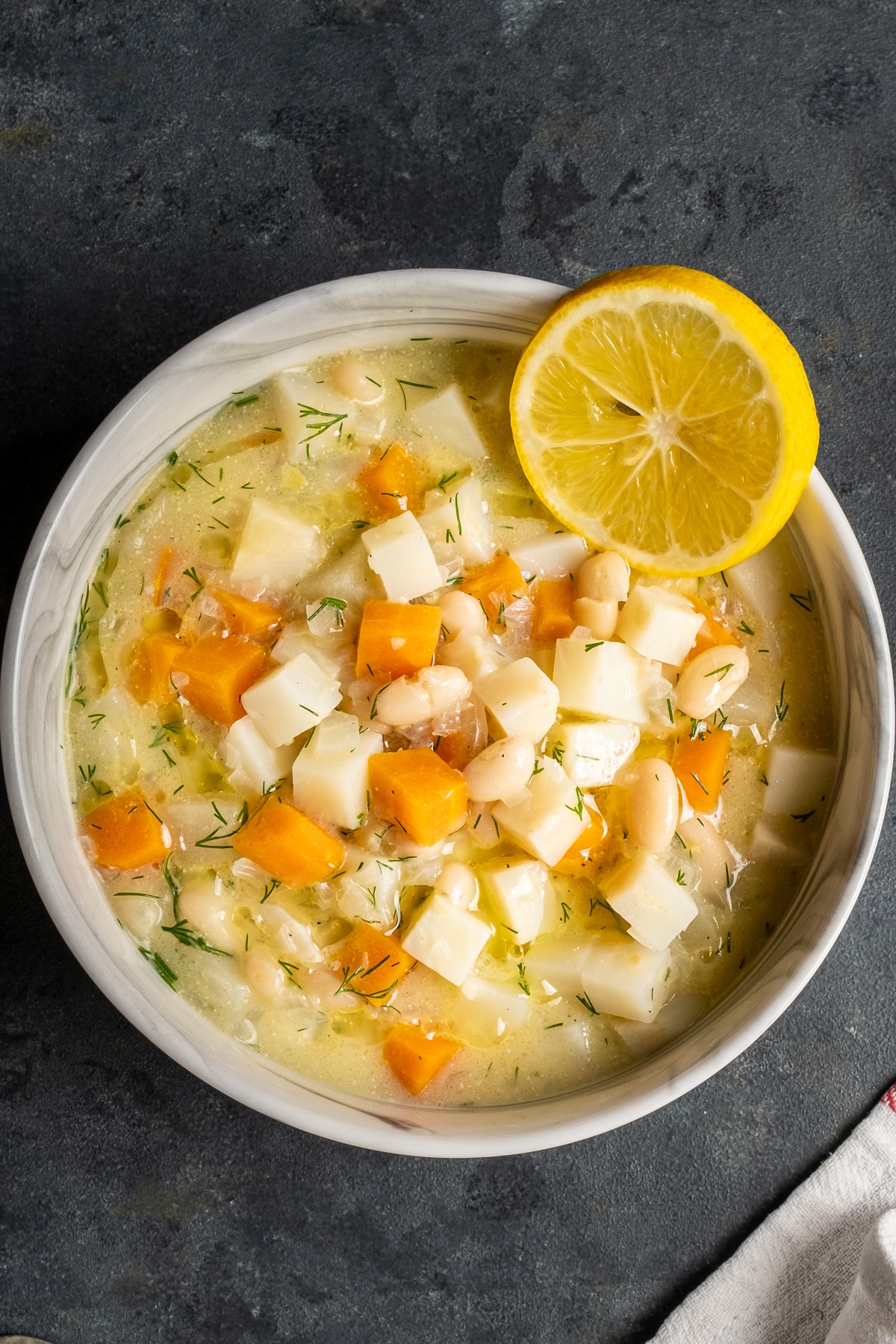 汤用celeriac，苹果，胡萝卜和豆子在一个白色的碗和碗的旁边柠檬切片。