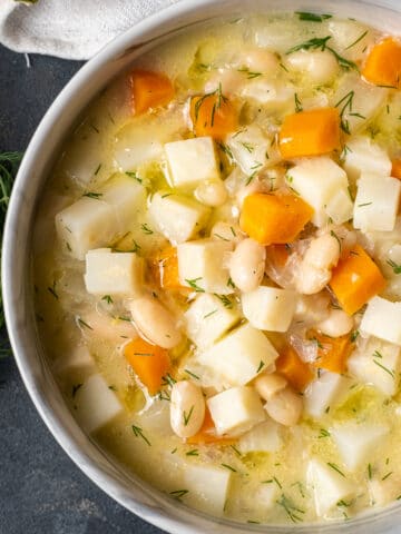 Celery root soup with apples, carrots and beans in a bowl on a dark background.