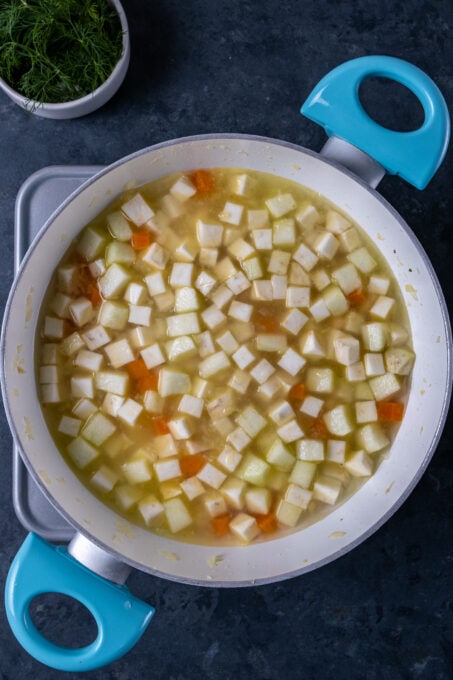 切成小块的芹菜根，红萝卜，苹果和水在白色平底锅。