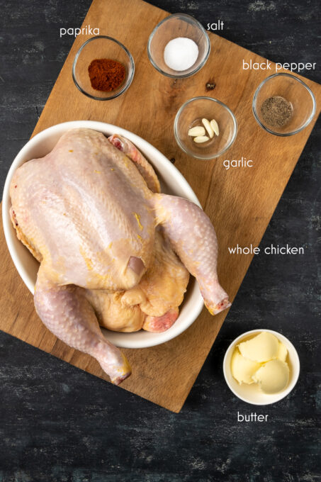 在平底锅，大蒜丁香，辣椒粉，盐，黑胡椒和黄油的未加工的整个鸡在一个木板的分开的碗。