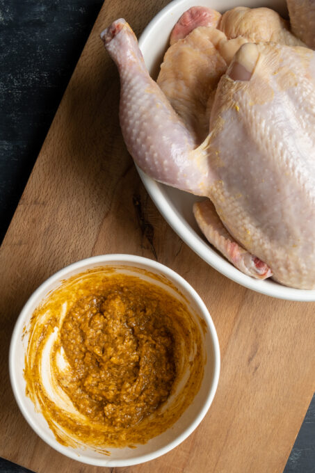 腌料用黄油和香料在一个白色碗和一个未加工的整鸡在一个平底锅在一个木板。