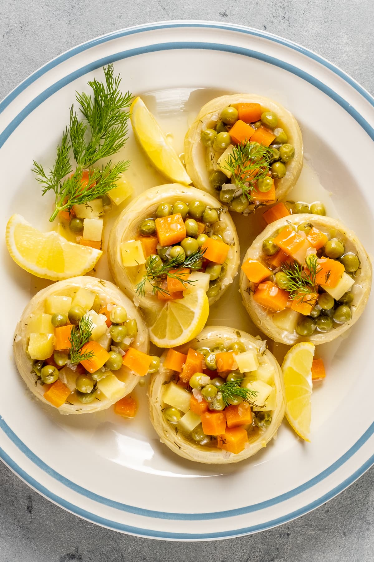 洋蓟底部塞满煮豌豆、土豆和胡萝卜配上柠檬和新鲜莳萝和蓝色条纹在白色的板。