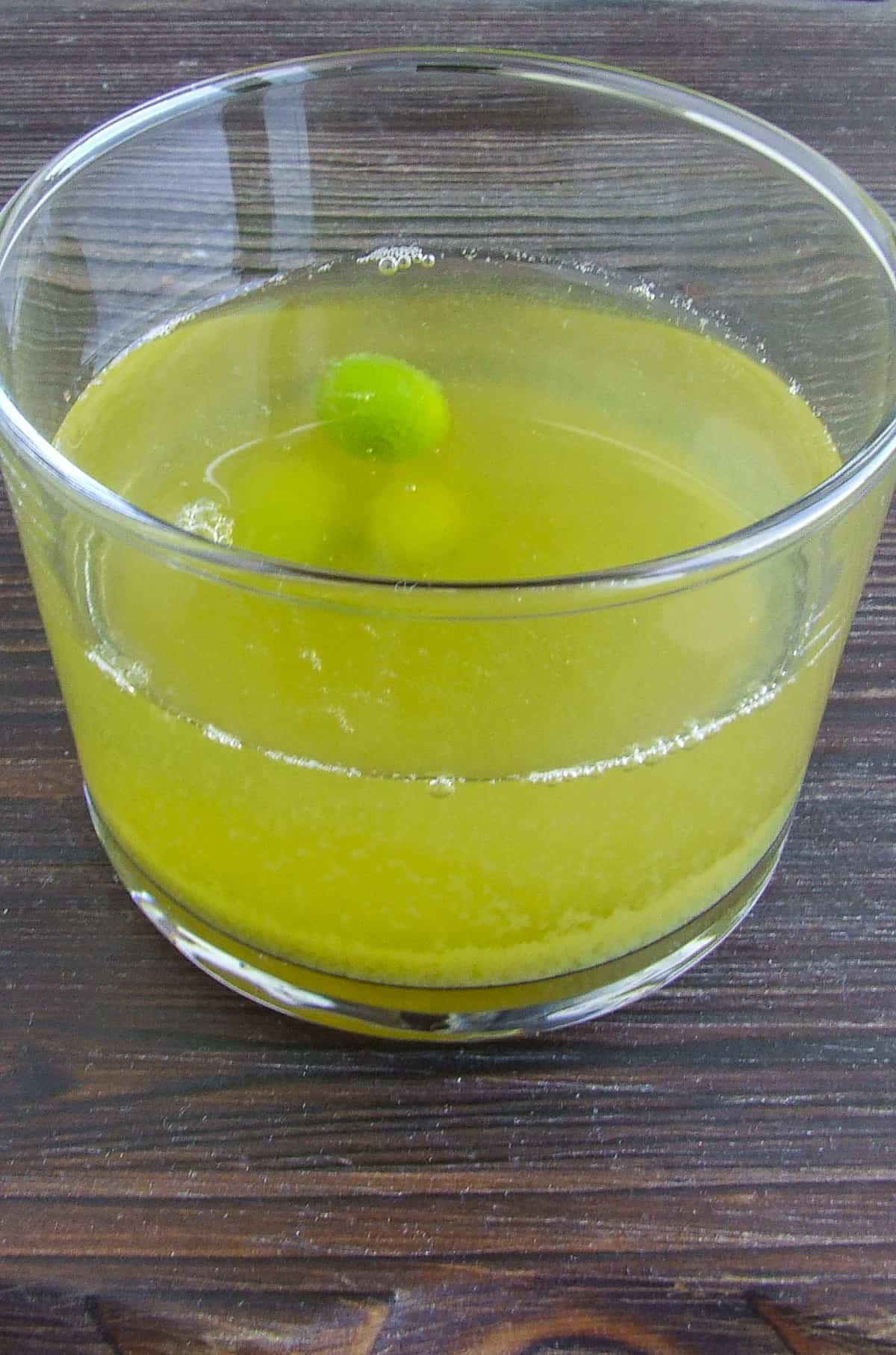 Fresh verjuice in a glass and an unripe grape in it.