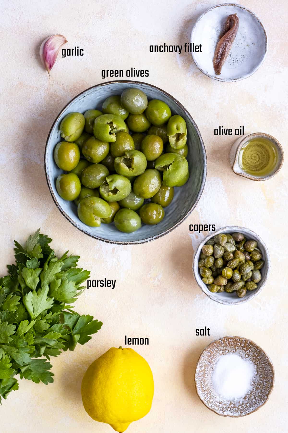 将青橄榄、酸豆、蒜瓣、凤尾鱼片、欧芹、柠檬、盐和橄榄油分别放入碗中。
