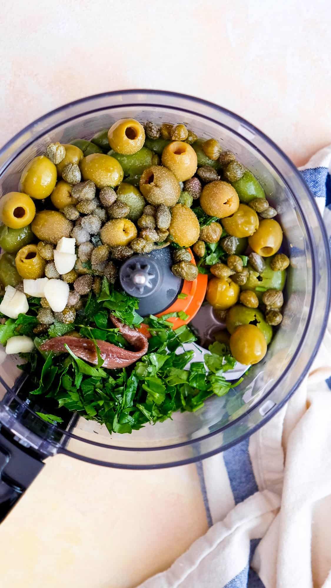 绿橄榄，欧芹，酸豆，大蒜，凤尾鱼片放入食品加工碗中。