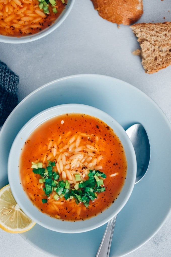 Turkish Tomato Orzo Soup Recipe packs a ton of flavor with fewer than 10 ingredients in just 20 minutes. The combination of tomatoes, lemon, parsley and orzo makes the easiest pasta soup ever. #orzosoup #wintersoup #souprecipe #turkishsoup 土耳其番茄汤配上欧芹,盛在浅蓝色的碗里,背景是灰色的。
