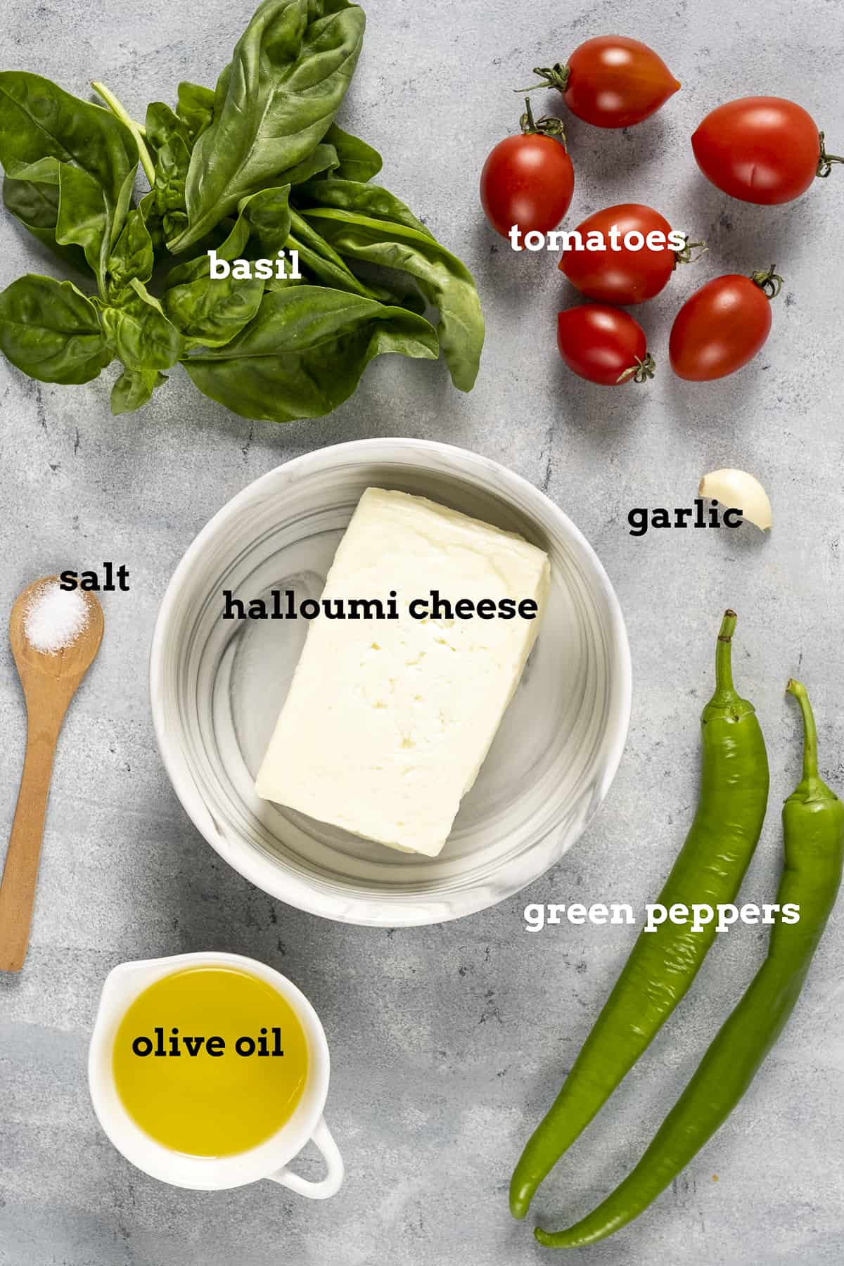 一块哈洛米奶酪、橄榄油、青椒、圣女果、罗勒和大蒜放在灰色的背景上。