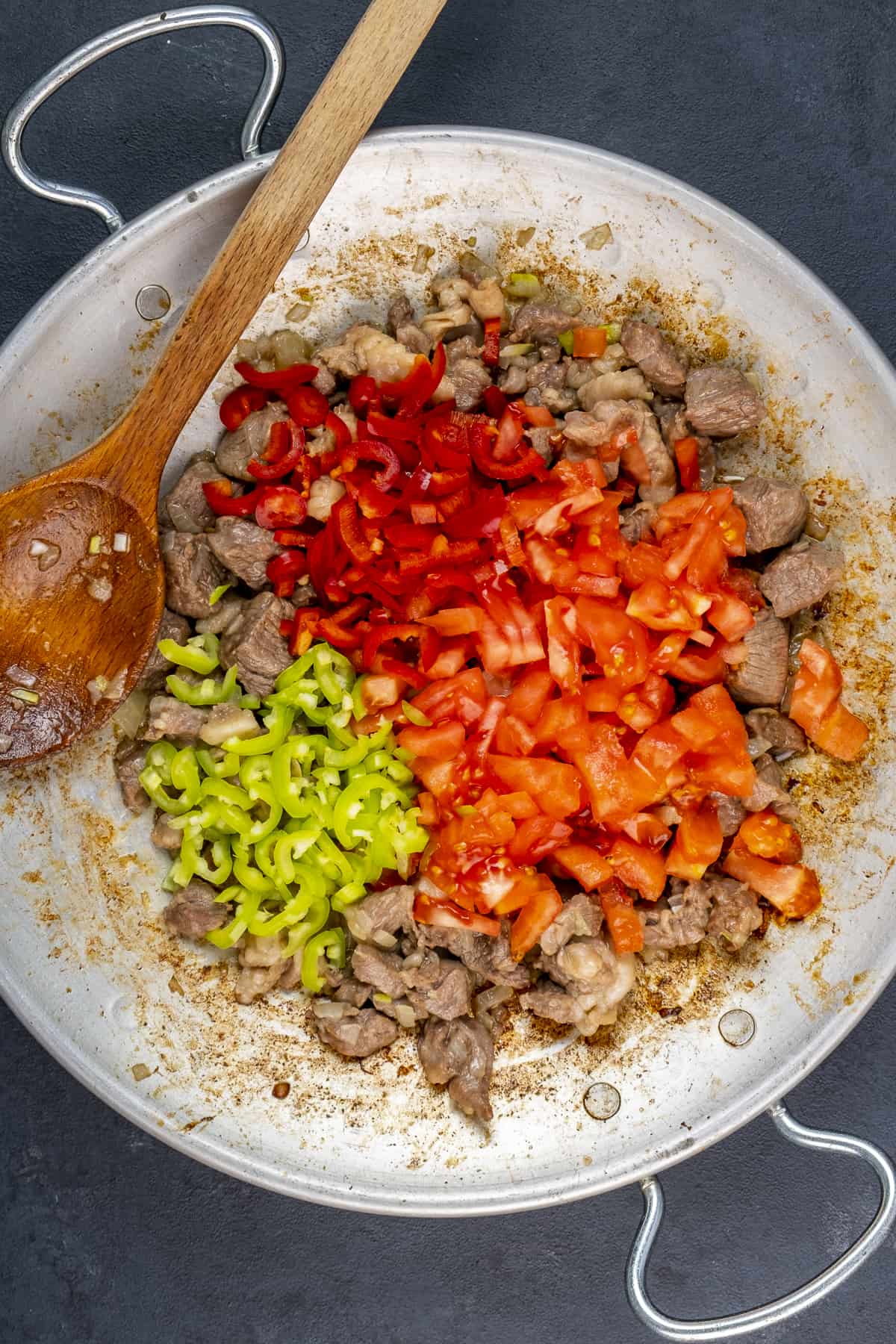 在传统的锅里，把切碎的西红柿和辣椒撒在煮熟的羊肉丁上。