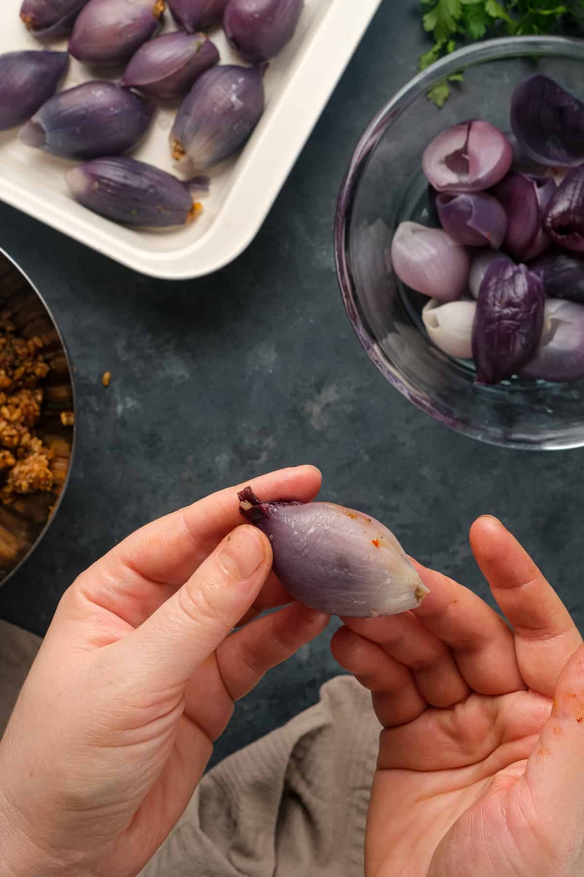 手拿一个紫洋葱馅和更多的洋葱馅放在平底锅里，盛在一个碗里，煮熟的洋葱放在另一个碗里。