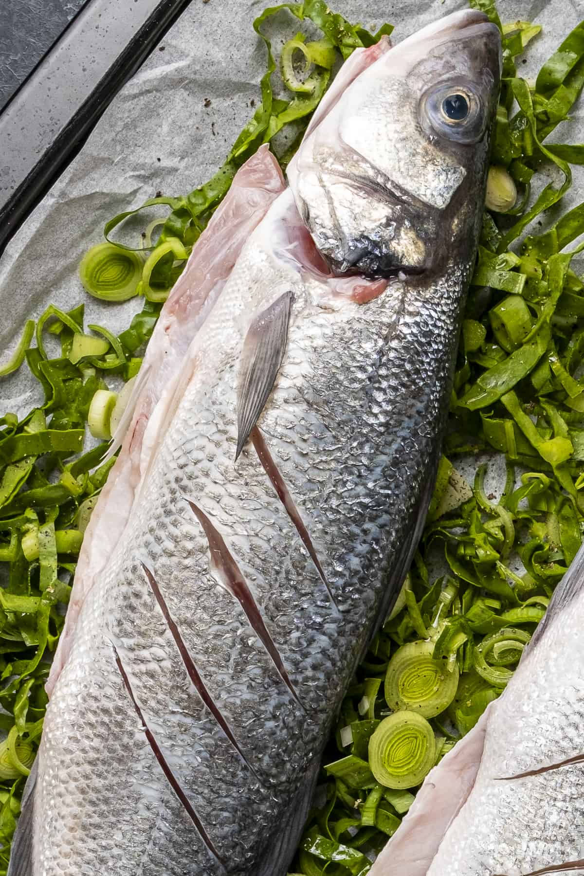 新鲜的整条海鲈鱼配上切碎的青菜。