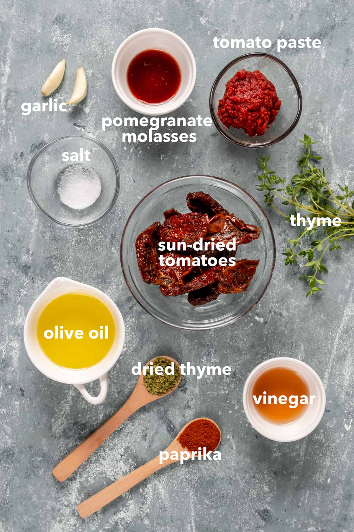 晒干的番茄、番茄酱、石榴糖浆、橄榄油、醋、香料、大蒜和新鲜的百里香放在灰色的背景上。