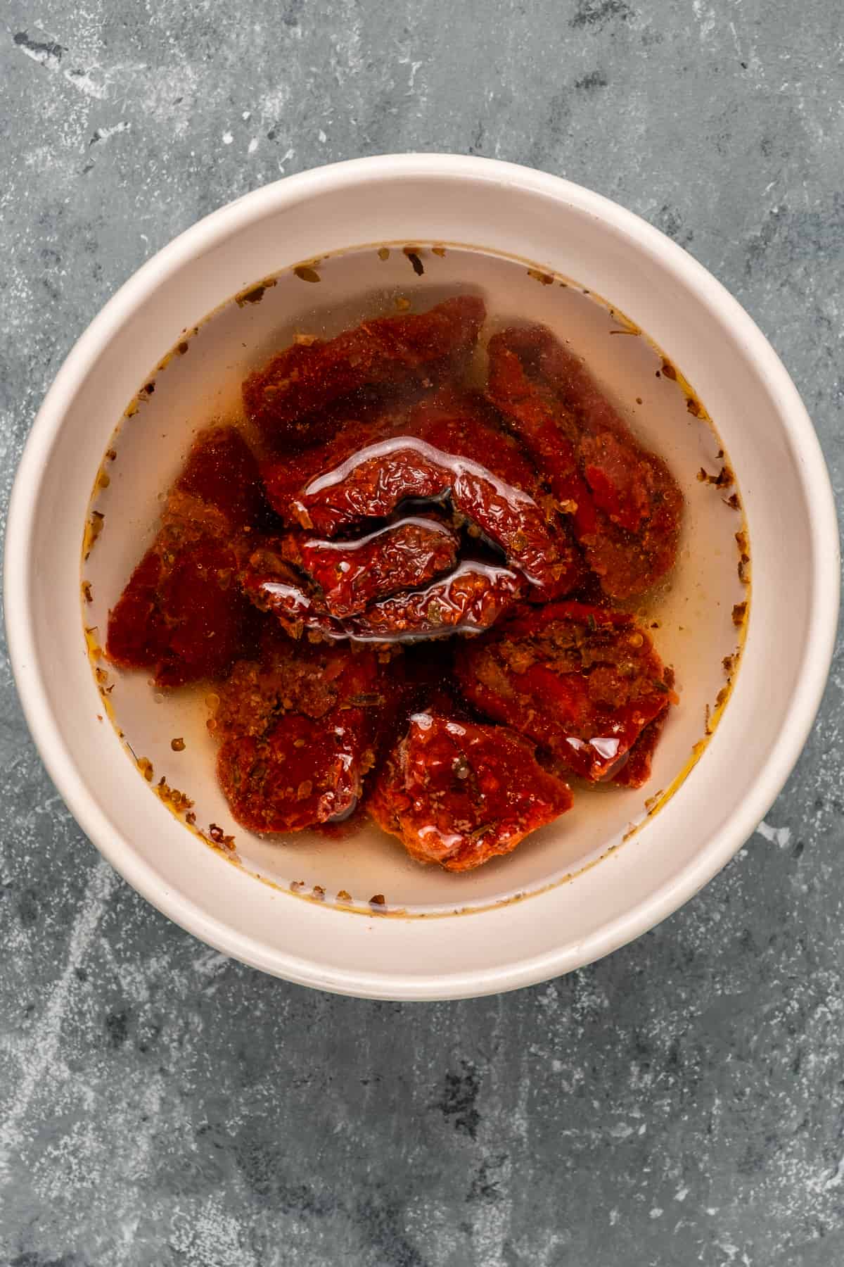 把晒干的西红柿浸泡在白色碗里,底色为灰色。