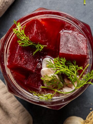 Chopped beets pickled in a jar, garnished with dill and garlic.