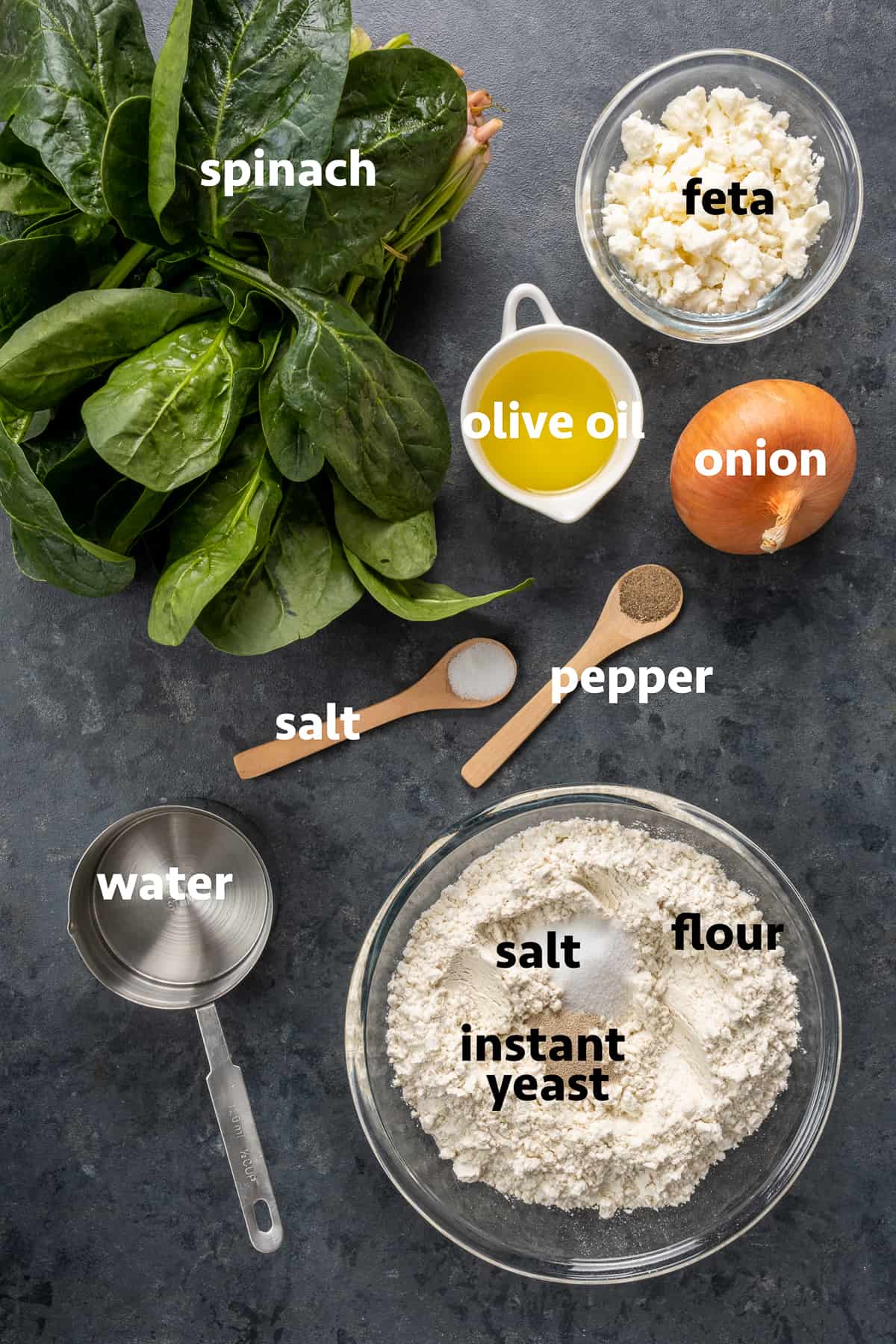 将Gozleme面团原料放入碗中，菠菜叶、橄榄油、洋葱、盐、胡椒粉和奶酪放在深色背景上。