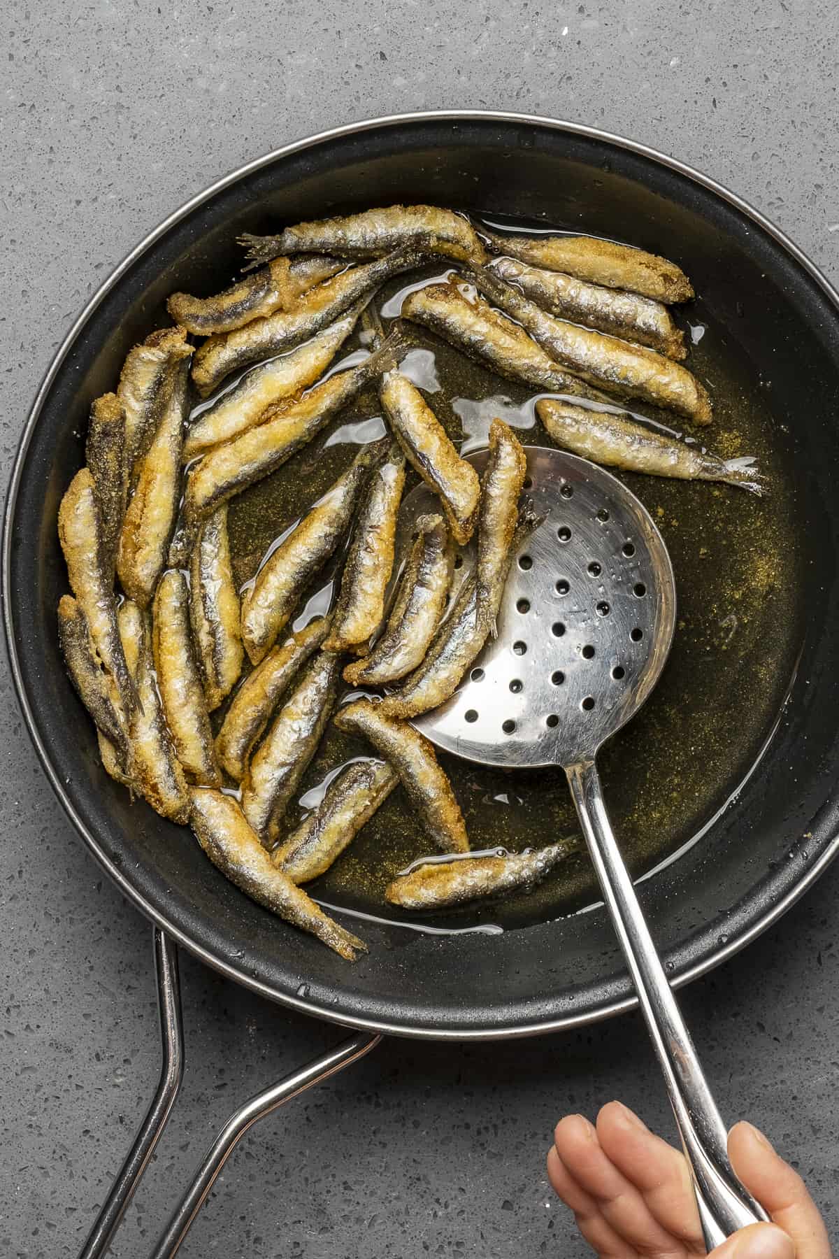 用漏勺从煎锅中取出煎过的凤尾鱼。