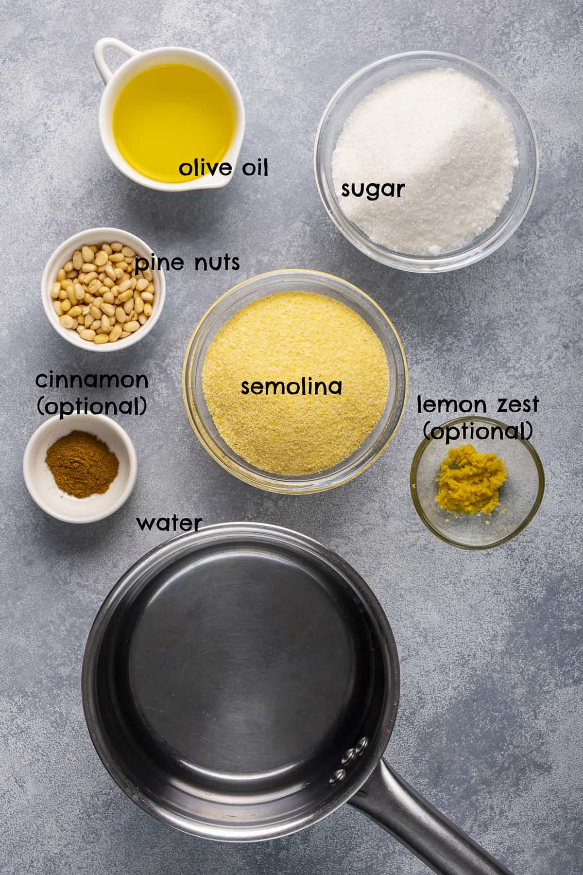 Semolina, pine nuts, sugar, oil, water, lemon zest, cinnamon pictured on a light background.