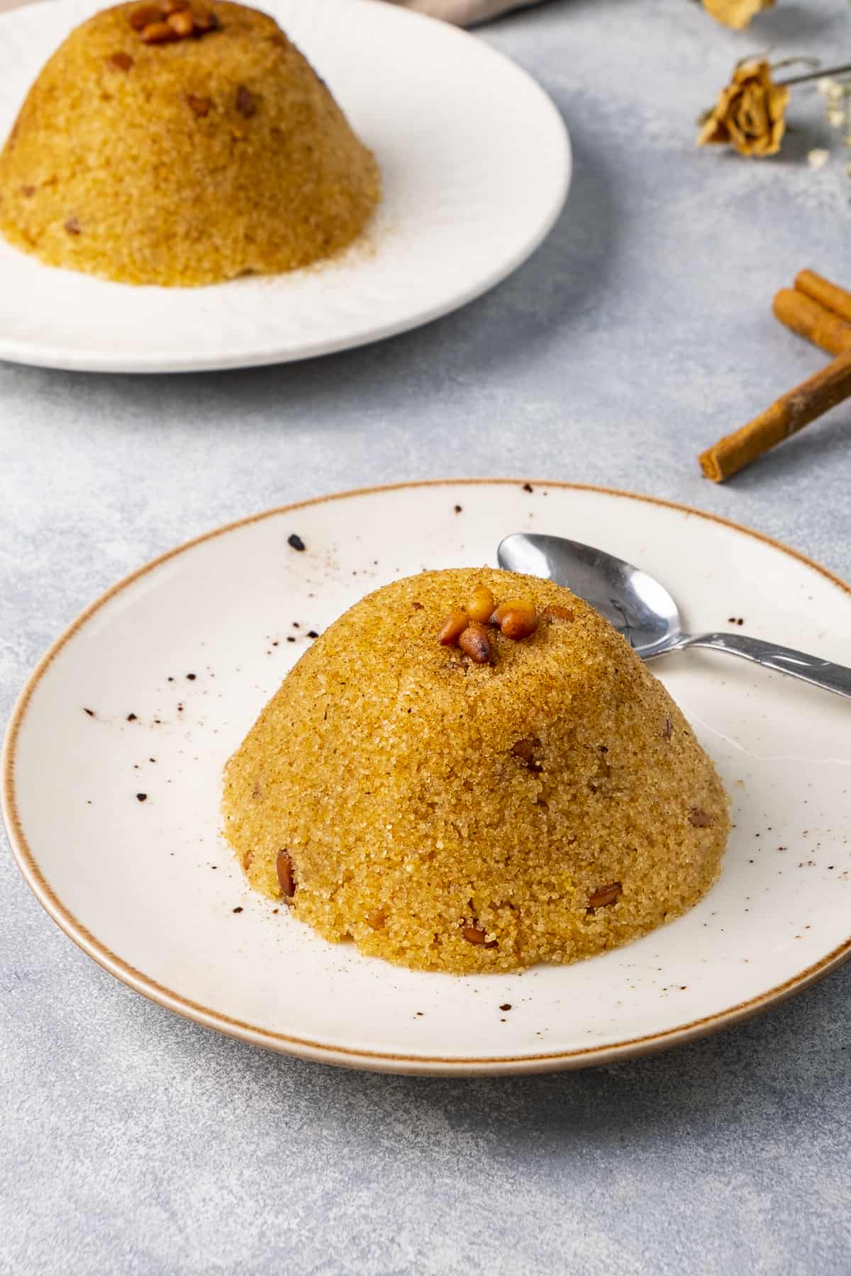 Semolina halva topped with pine nuts on two white plates.