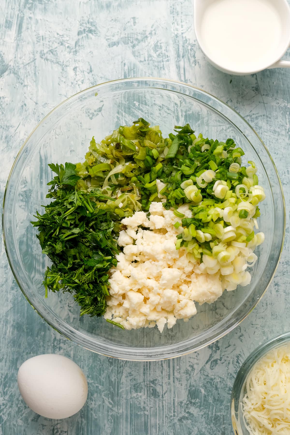 煮熟的韭菜，大葱，香草和奶酪在一个玻璃碗在浅色背景。