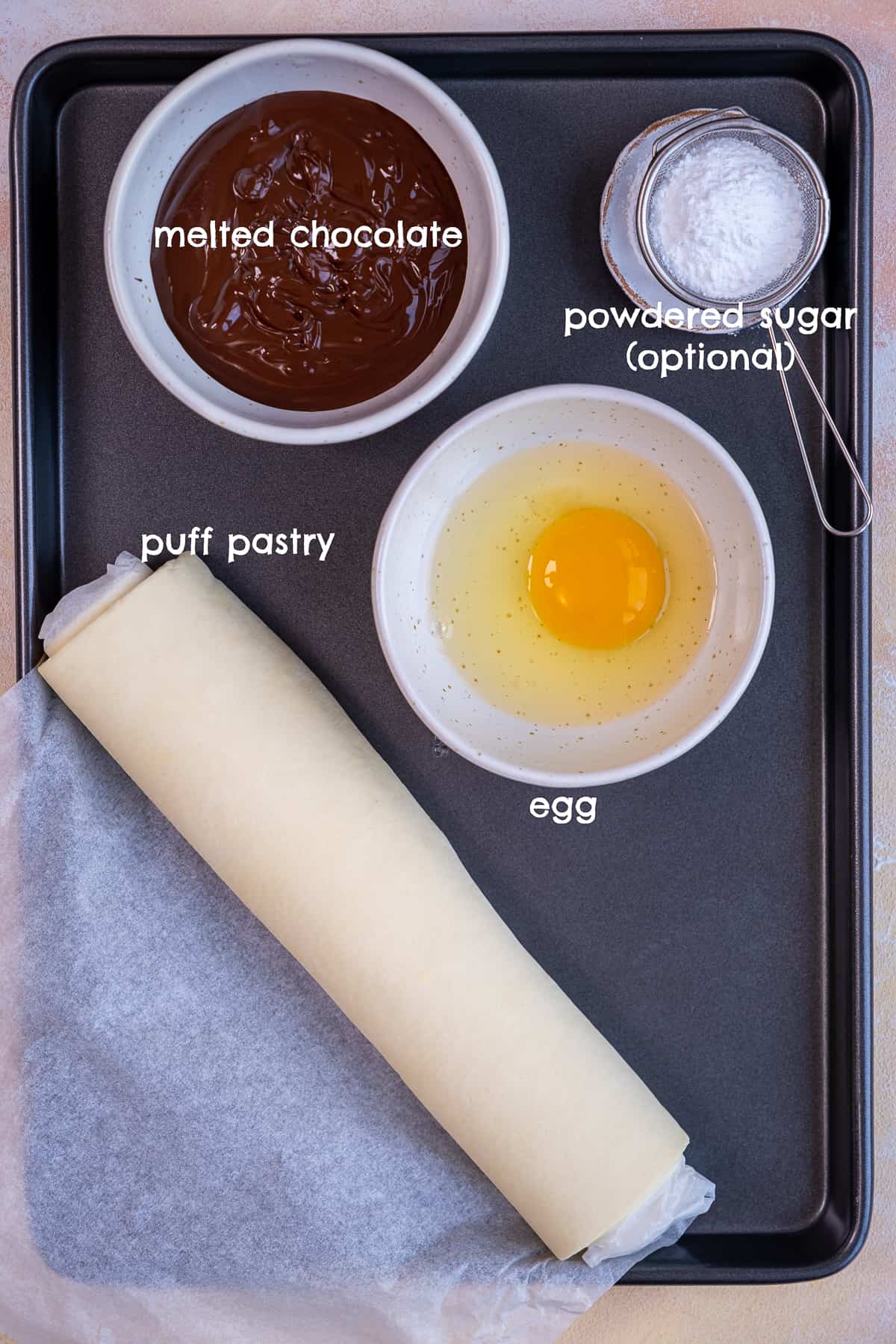 融化的巧克力、酥皮、鸡蛋和糖粉放在烤盘上拍照。