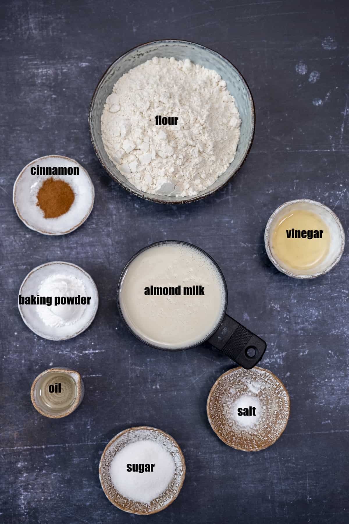 杏仁奶、醋、油、面粉、肉桂、糖、盐和发酵粉放在不同的碗里，背景要暗。