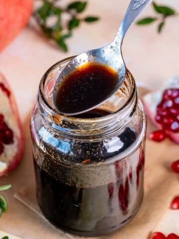 Pomegranate molasses in a jar and a spoon on its top.