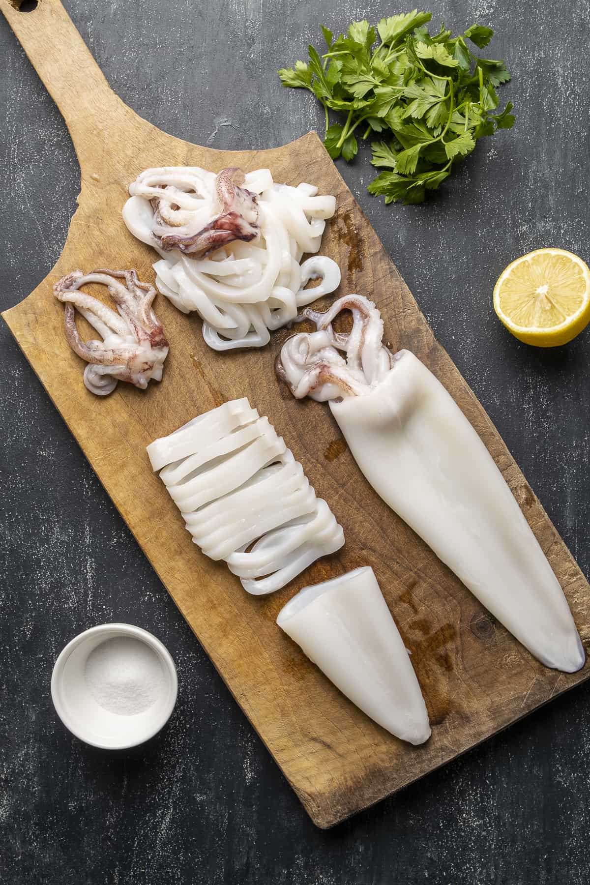 整只鱿鱼放在砧板上，切成半片，撒上欧芹和柠檬。